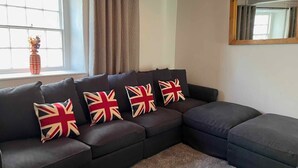 Un canapé modulable agrémenté de quatre coussins aux couleurs du drapeau britannique, une fenêtre avec des rideaux et un miroir accroché au mur.