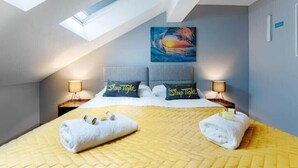 Un dormitorio con tragaluz, una cama con almohadas que dicen 'Sleep Tight', un cuadro en la pared y dos lámparas de noche.