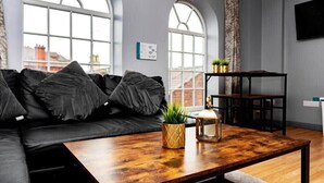 Una sala de estar moderna con un sofá de cuero negro, una mesa de centro de madera y ventanas amplias con arcos.