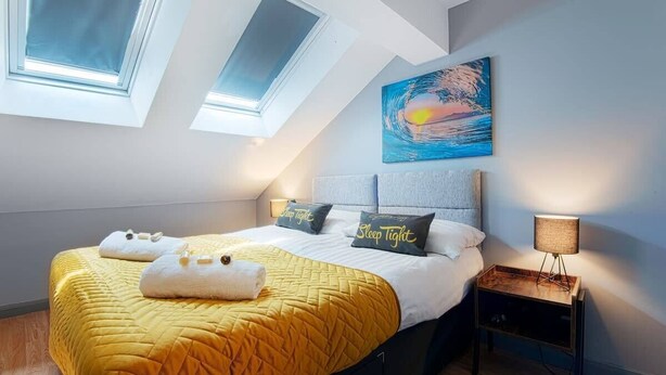 Un dormitorio con una cama, dos tragaluces, un cuadro y una lámpara de noche.