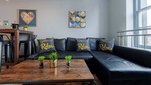 Una sala de estar moderna con un sofá de cuero negro, una mesa de centro de madera con plantas y obras de arte en las paredes.