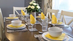 A dining table set with white bowls, yellow napkins, and clear glasses, with a vase of white flowers in the center. - The Flintshire - 3 Bedroomed House - Flint (Flint)