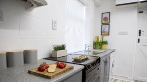 A modern kitchen with a granite countertop, a built-in stove, and a dishwasher. There are grey storage bins on the counter, a potted plant, and a cutting board with tomatoes and cheese. - The Flintshire - 3 Bedroomed House - Flint (Flint)