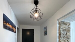 Een gang met een zwarte deur, een houten console tafel met manden, een stenen muur en een geometrisch lamp.