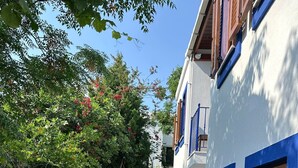 A narrow stone-paved alley with a stone wall on one side and a white building with blue trim and wooden shutters on the other. - Wish Suites Bodrum Hotel (Bodrum)