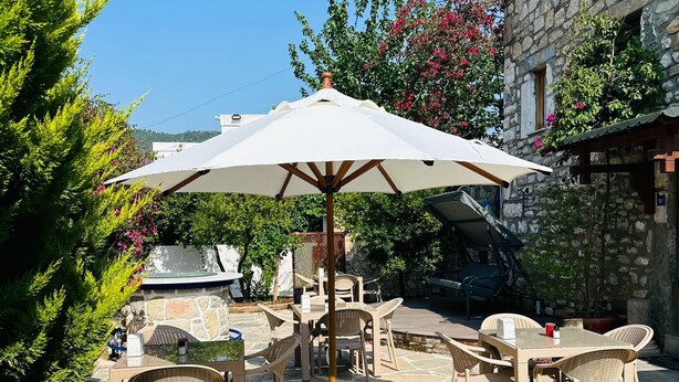 An outdoor patio with stone flooring, wicker furniture, and a white umbrella. - Wish Suites Bodrum Hotel (Bodrum)