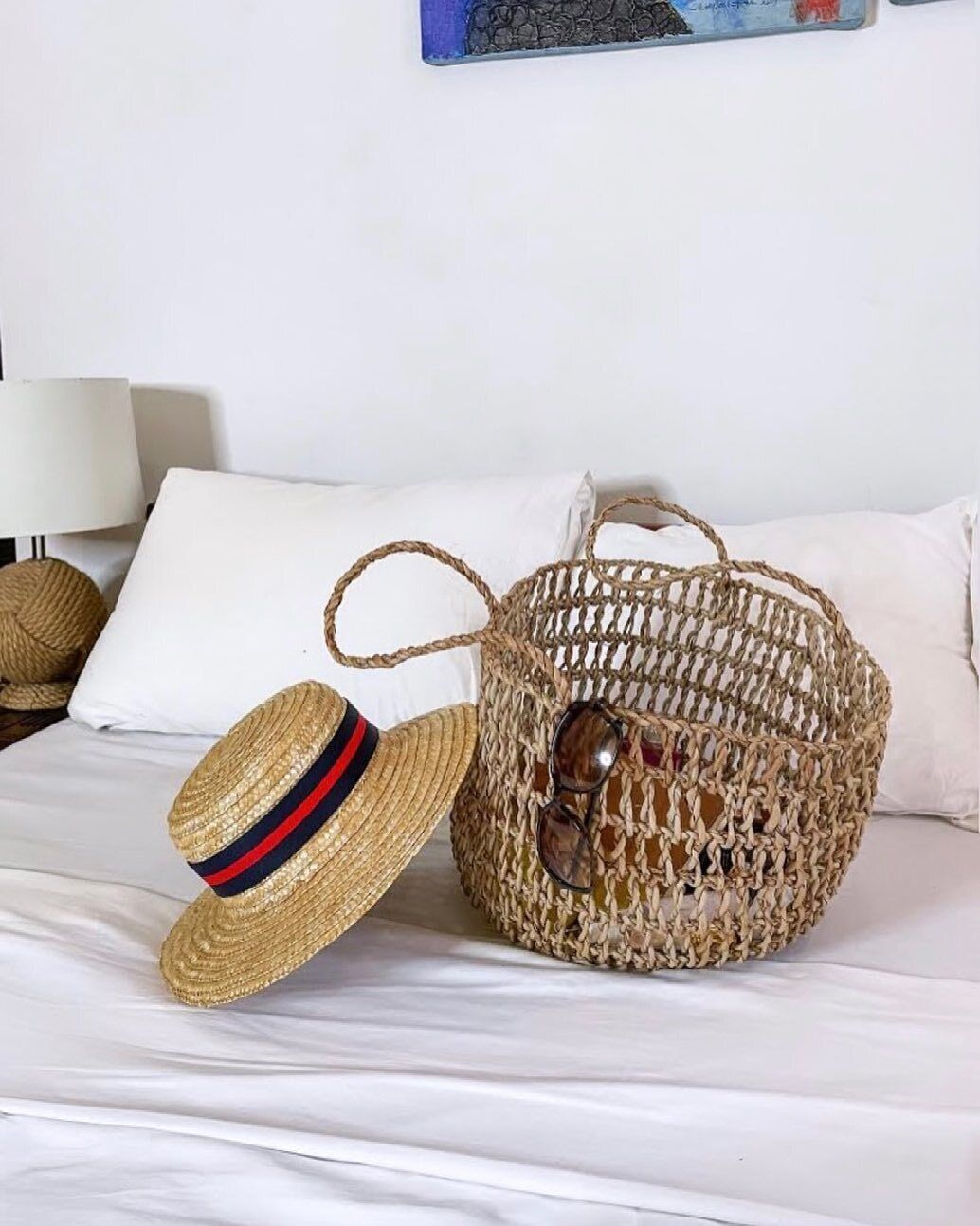 A woven basket with a handle on a bed.