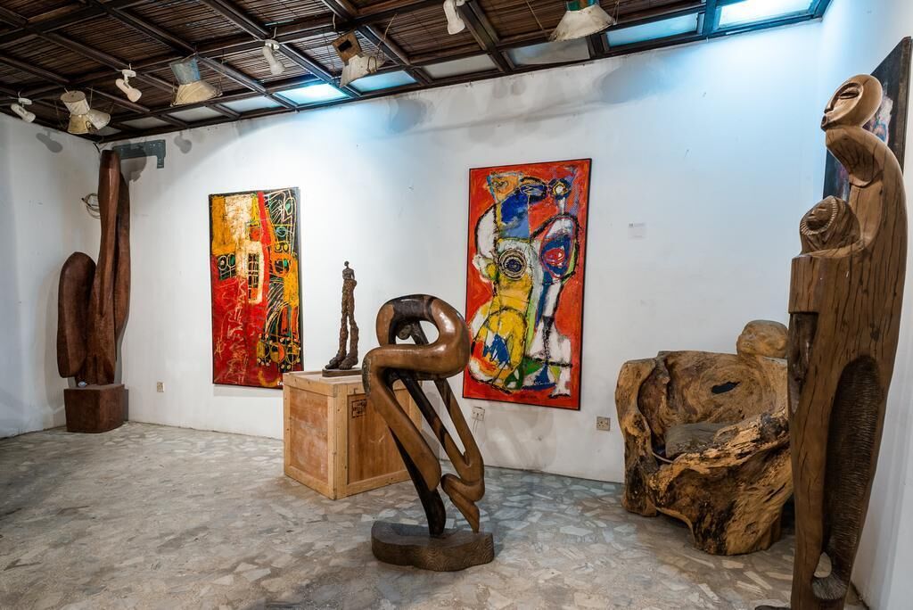 Een kunstgalerie met houten sculpturen en schilderijen aan de wanden.