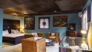 Une pièce comprenant un lit, des meubles en osier, une table basse en verre et des œuvres d’art accrochées aux murs.