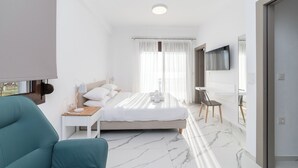 A modern hotel room with a bed, a desk, a chair, a TV, and a bathroom. - Argilos & Argilos Deluxe Residential Complexes-Two - Bedroom Duplex with Garden (Kavala)