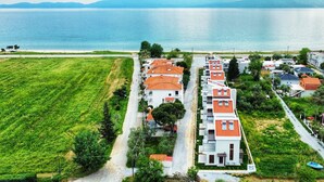 A coastal residential area with houses featuring red-tiled roofs, a grassy field, and a view of the sea. - Argilos & Argilos Deluxe Residential Complexes-Two - Bedroom Duplex with Garden (Kavala)