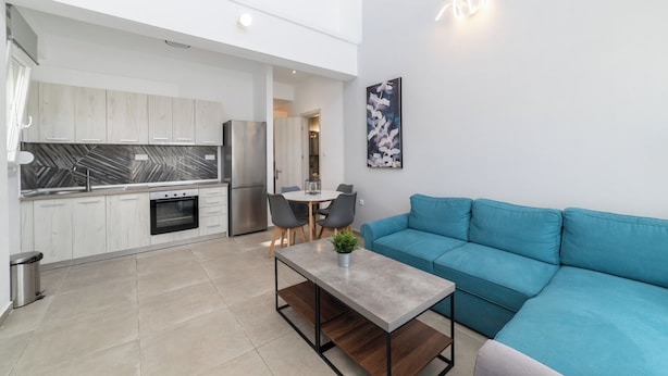 A modern kitchen with a marble backsplash, a dining area with a table and chairs, and a teal sofa.