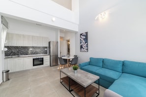 A modern kitchen with a marble backsplash, a dining area with a table and chairs, and a teal sofa. - Thalassa- Two-Bedroom Duplex with Garden (Kavala)