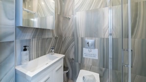 A modern bathroom with marble walls, a white sink, and a glass shower enclosure.