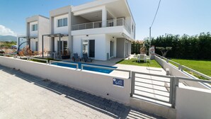 Una casa moderna de dos pisos con piscina, mobiliario exterior y vista al mar.