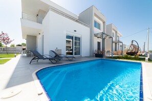 Ein modernes Gebäude mit Schwimmbad, Außenbereich mit Sitzgelegenheiten und einem Garten.