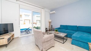 Una sala moderna con una televisión de pantalla plana, un sillón beige, un sofá azul y una mesita de noche con una lámpara.
