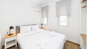 Une chambre d’hôtel au design minimaliste, comprenant un lit, des tables de chevet, un bureau et une fenêtre avec des stores.