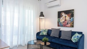 Een moderne woonkamer met een donkerblauwe bank, twee ronde tafels, en een groot schilderij van een tropische vogel aan de muur.
