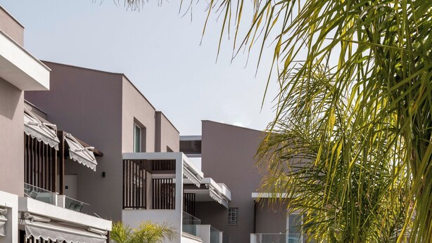 Un espacio exterior moderno con piscina, mobiliario blanco y un jardín bien cuidado.