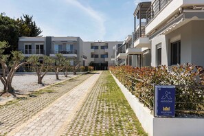 Um edifício residencial moderno com um caminho pavimentado, árvores e uma placa para Antigone Kourtidis Group.