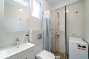 Uma casa de banho moderna com lavatório, sanita e chuveiro brancos.