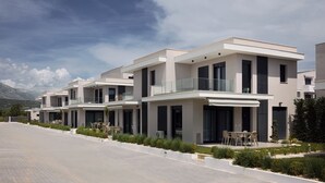 A modern residential building with multiple balconies, large windows, and a paved driveway. - Nefeli Residential Complex-One Bedroom Apartment (Kavala)