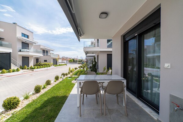 A modern outdoor patio with a table and chairs, a glass door, and a view of a residential street.