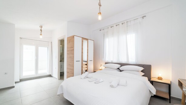 Un dormitorio moderno con una cama grande, un armario, un escritorio y un baño visible a través de una puerta abierta.