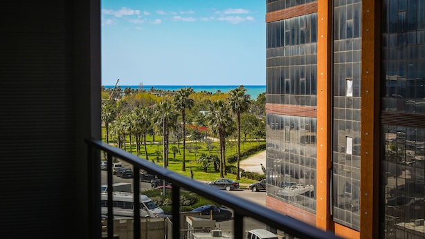 A view from a balcony overlooking a parking lot, a green lawn, and a building with large windows. - New wave apart hotel (Batumi)