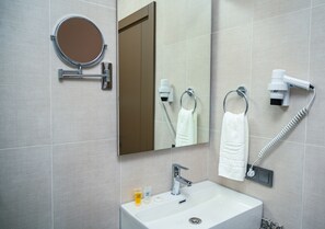 A bathroom with a sink, mirror, towel rack, hairdryer, and toiletries. - New wave apart hotel (Batumi)
