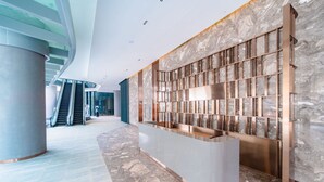 A modern reception area with a marble wall, a reception desk, and an escalator in the background. - Ha Long Bay Luxury Homestay (Bai Chay)