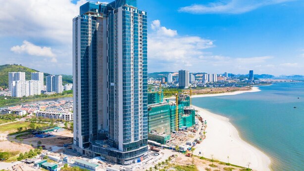 A high-rise building with a modern glass facade, situated near a beach with clear blue waters. - Ha Long Bay Luxury Homestay (Bai Chay)