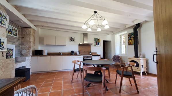Una cocina compacta con armarios blancos, un comedor con mesa y sillas redondas, y una lámpara colgante.