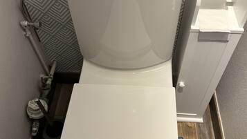 Eine weiße Toilette mit Tank und Sitz, einem Toilettenpapierhalter und einem sichtbaren Abwasserrohr.