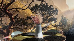 Uma sala de jantar com uma mesa redonda, cadeiras e um vaso com flores.