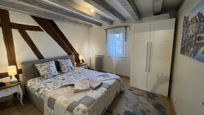 Quarto com cama, mesa de cabeceira, luminária, guarda-roupa e janela com cortinas.