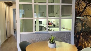 Cozinha moderna com ilha central, área de jantar com mesa e cadeiras redondas e um mural decorativo de árvore na parede.