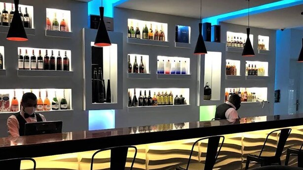 A bar area with shelves of bottles, a counter, and bar stools. - Quintessential Hotel Port Harcourt (Port Harcourt)