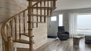 Eine hölzerne Wendeltreppe in einem Raum mit einem grauen Sessel und einem Holztisch.