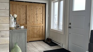 Ein Flur mit einer Holztür, einem grauen Schrank mit einer grünen Vase und einer schwarzen Matte, die zu einer weißen Tür führt.