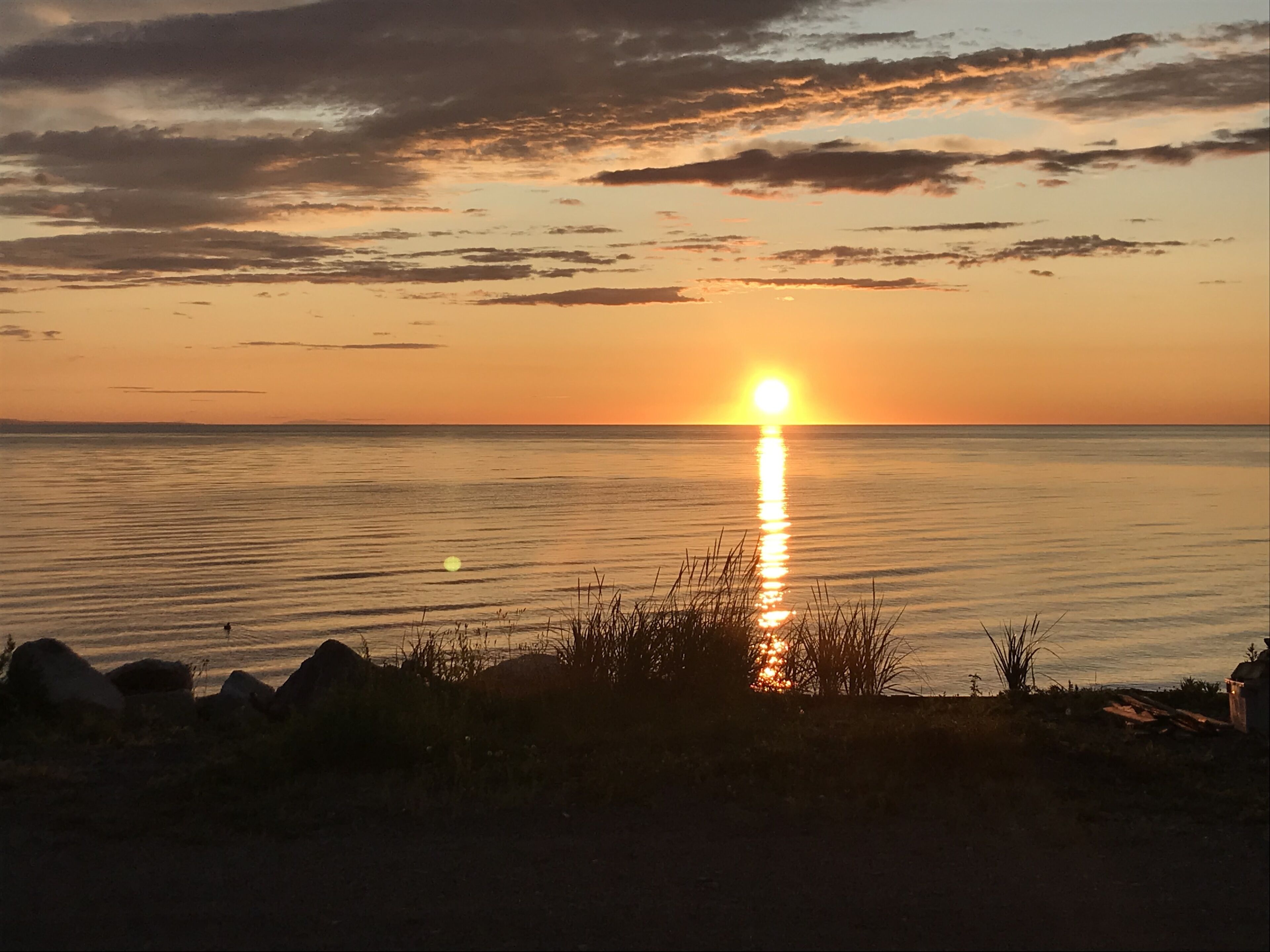 A sunset over a calm body of water with a rocky shoreline in the foreground.