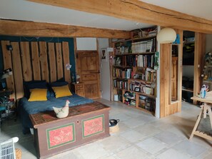 Ein gemütliches Schlafzimmer mit einem hölzernen Kopfteil, einem Bett mit blau-gelber Bettwäsche, einer Holzkommode und einem Bücherregal voller Bücher.
