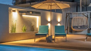 Zona junto a la piscina con dos sillas, una silla colgante e iluminación montada en la pared.