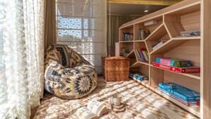 A cozy reading nook with a patterned bean bag, a bookshelf with board games, and a patterned rug. - Celestial Rhapsody (Nainital)