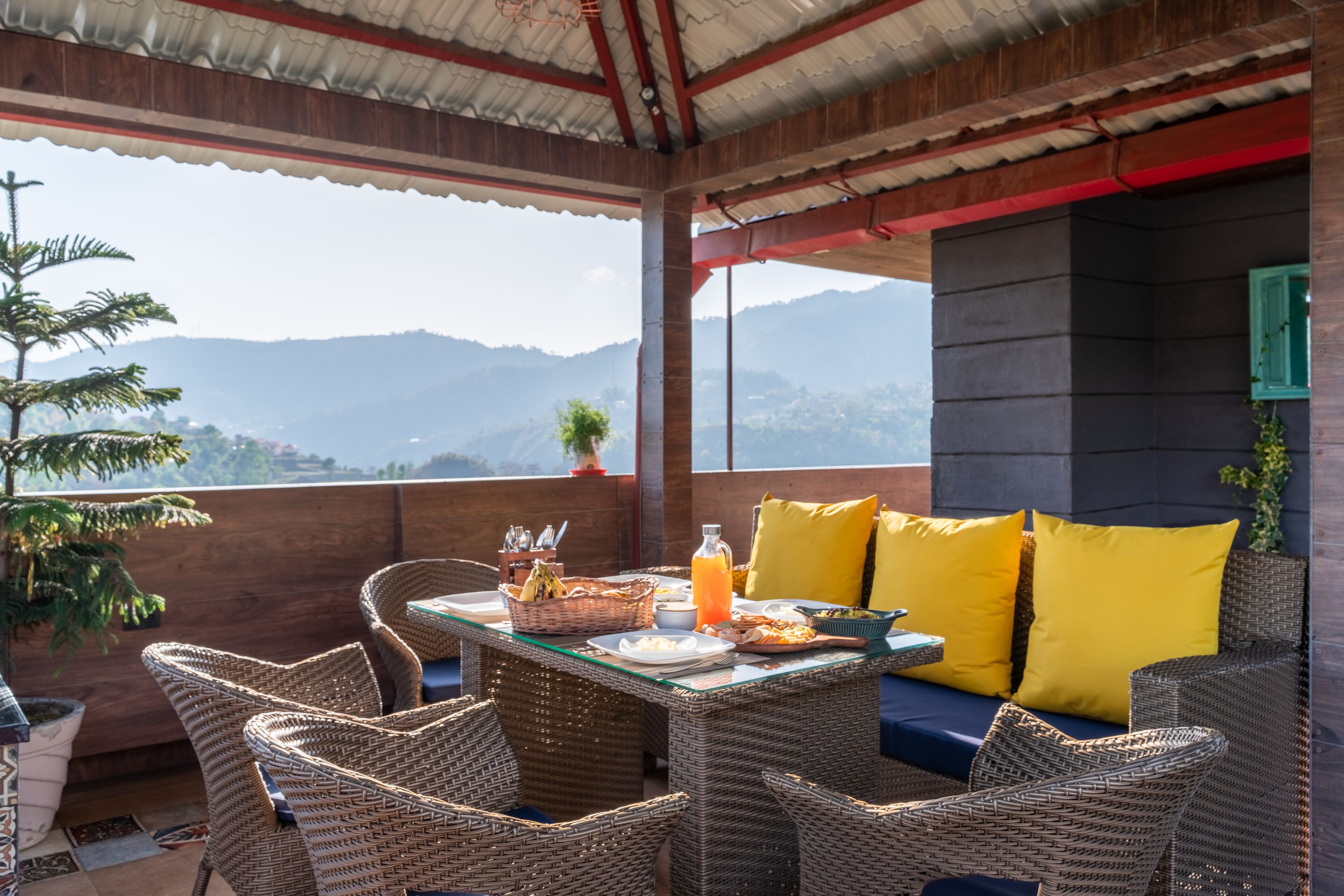 Un espace extérieur aménagé pour les repas, avec des meubles en osier, une table en verre et une vue sur les montagnes.