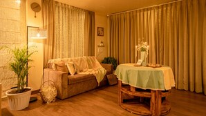 A cozy living room with a sofa, a dining table with a tablecloth, a potted plant, and curtains. - Celestial Rhapsody (Nainital)