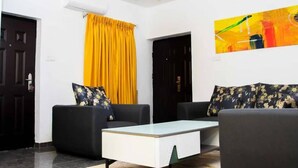 A modern living room with two black sofas, a white coffee table, and a yellow curtain. - Delight Apartments Oniru VI (Lagos)