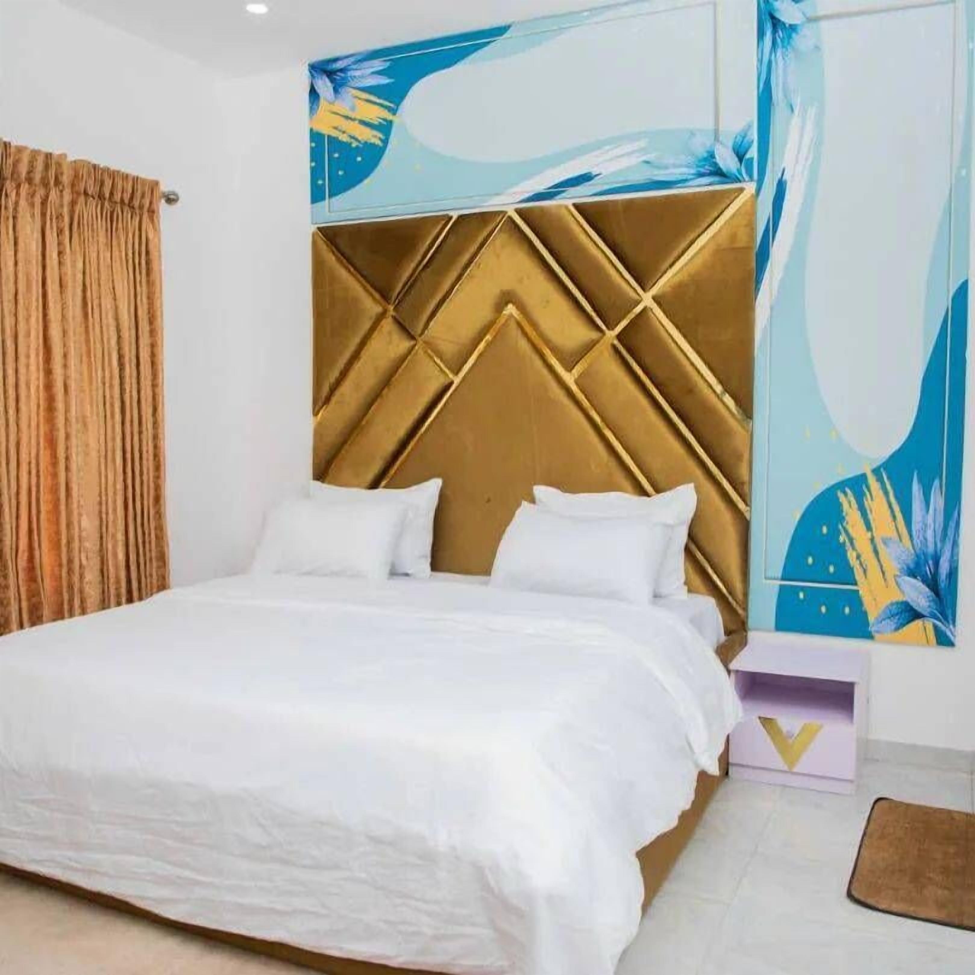 A modern bedroom with a large bed, a decorative headboard, and a wall mural.