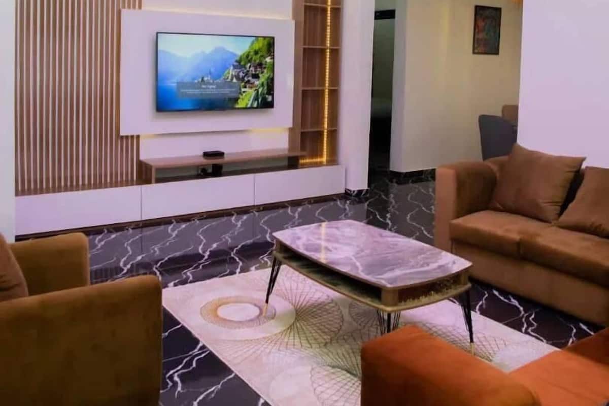 A modern living room with a flat-screen TV, a chandelier, and a sofa.